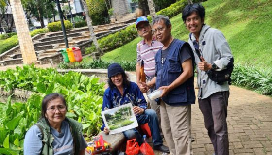 Dicksy Iskandar duduk memegang lukisan hasil karya bimbingannya.